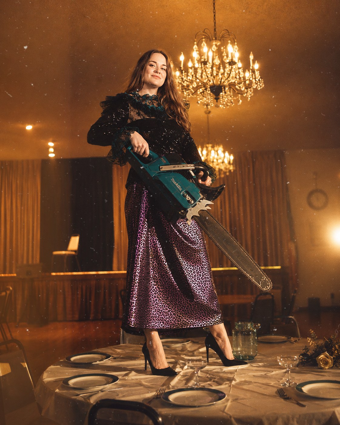 Malin Frithiofsson standing on a banquet table in a ballroom, holding a chainsaw
