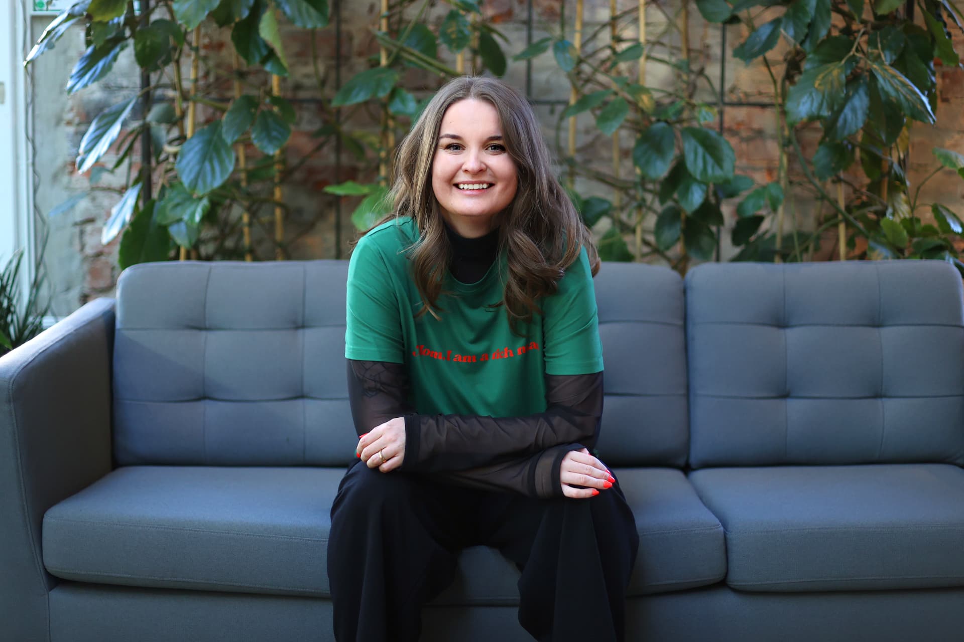 Malin Frithiofsson sitting on a sofa, smiling, wearing a green t-shirt
